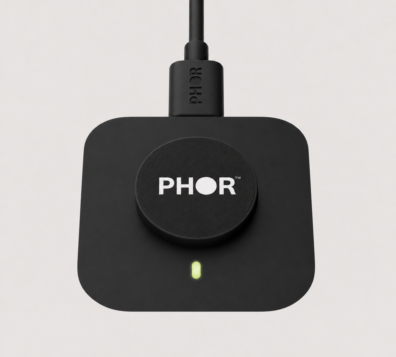 Matte black PHOR charging dock with the PHOR wordmark on its circular platform and a USB-C cable
